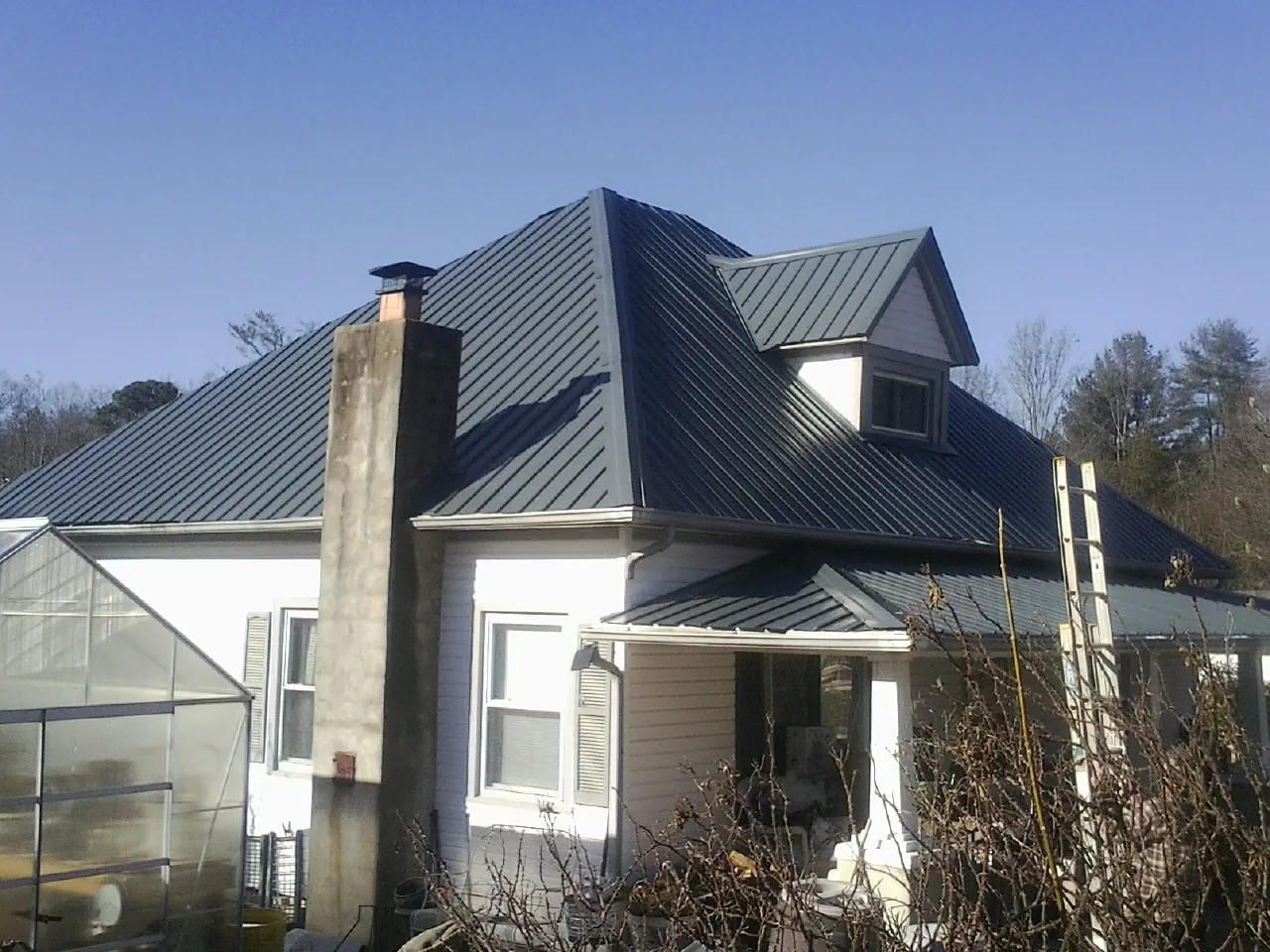 Dark blue standing seam metal roof on a white farmhouse with dormer — Slate & Tile Roof Repair by Roofing Brothers in Haskell