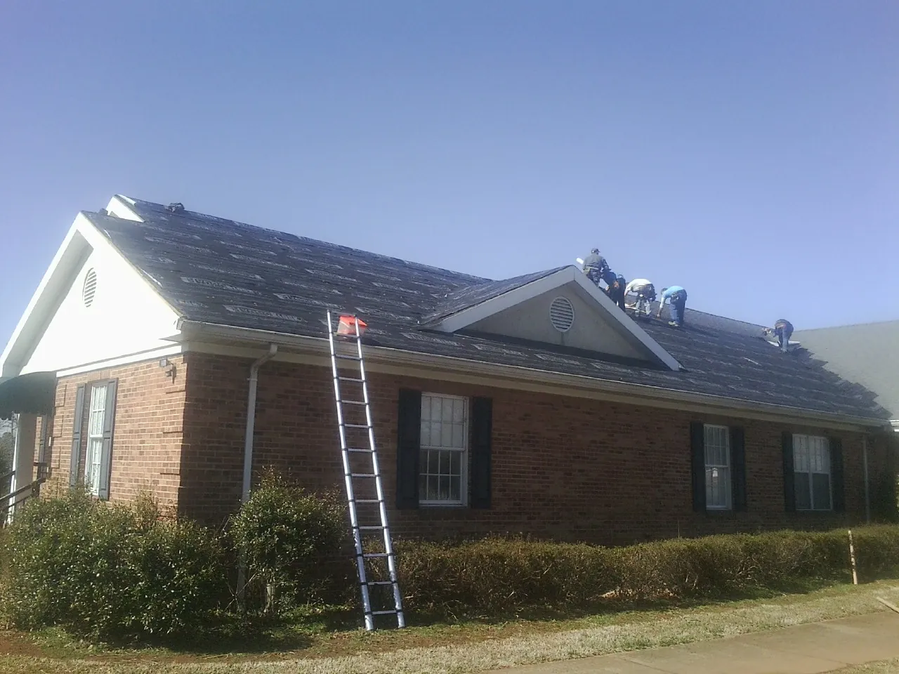 Crew tearing shingles off a brick ranch roof with a ladder set — Emergency Roof Repair work by our crew in Haskell