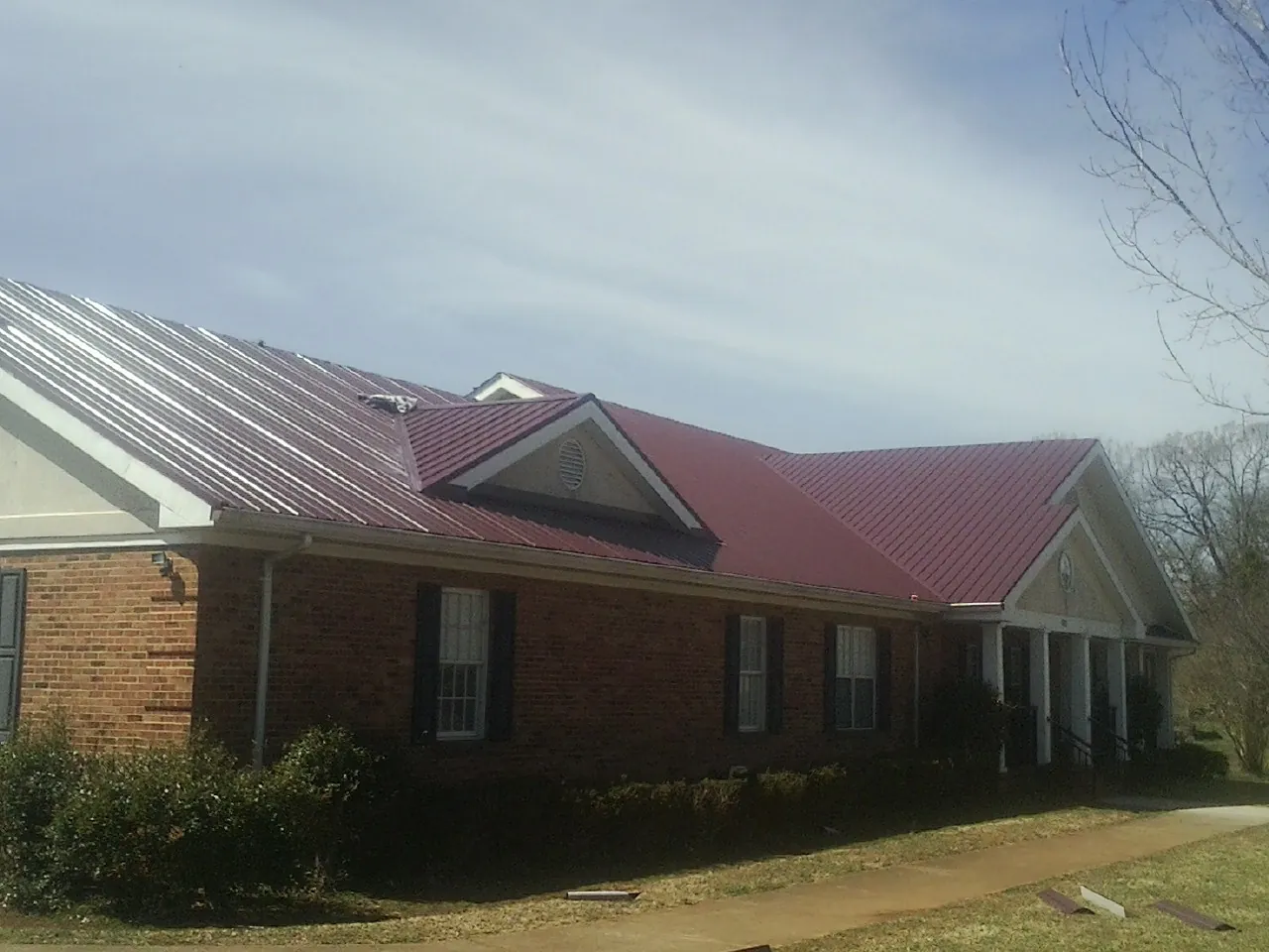 Red metal roof with gabled entries on a long brick building, from a Hail Damage Roof Repair job in Haskell
