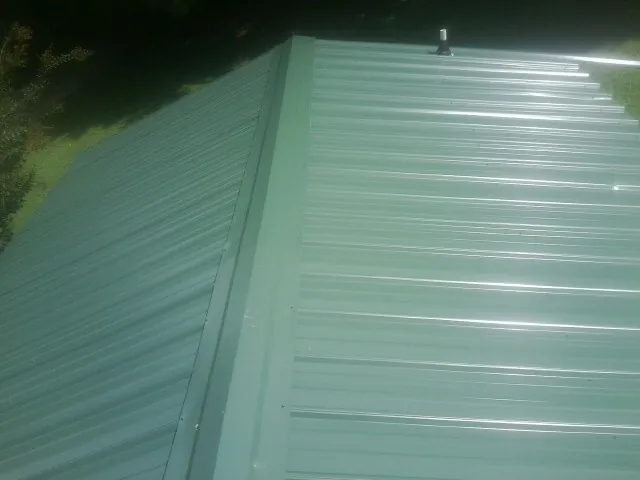 New green metal panels meeting at the ridge of a roof — Flat Roof Repair work by our crew in Haskell