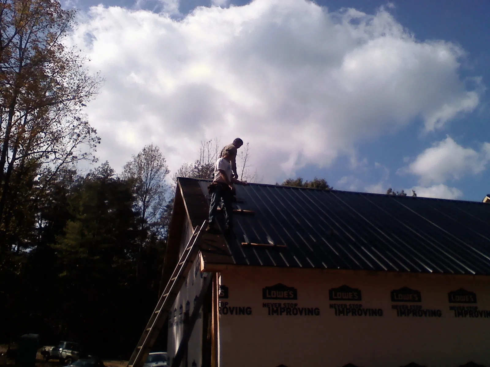 Roofer fastening dark metal panels high against a cloudy sky, from a Roof Inspection job in Haskell