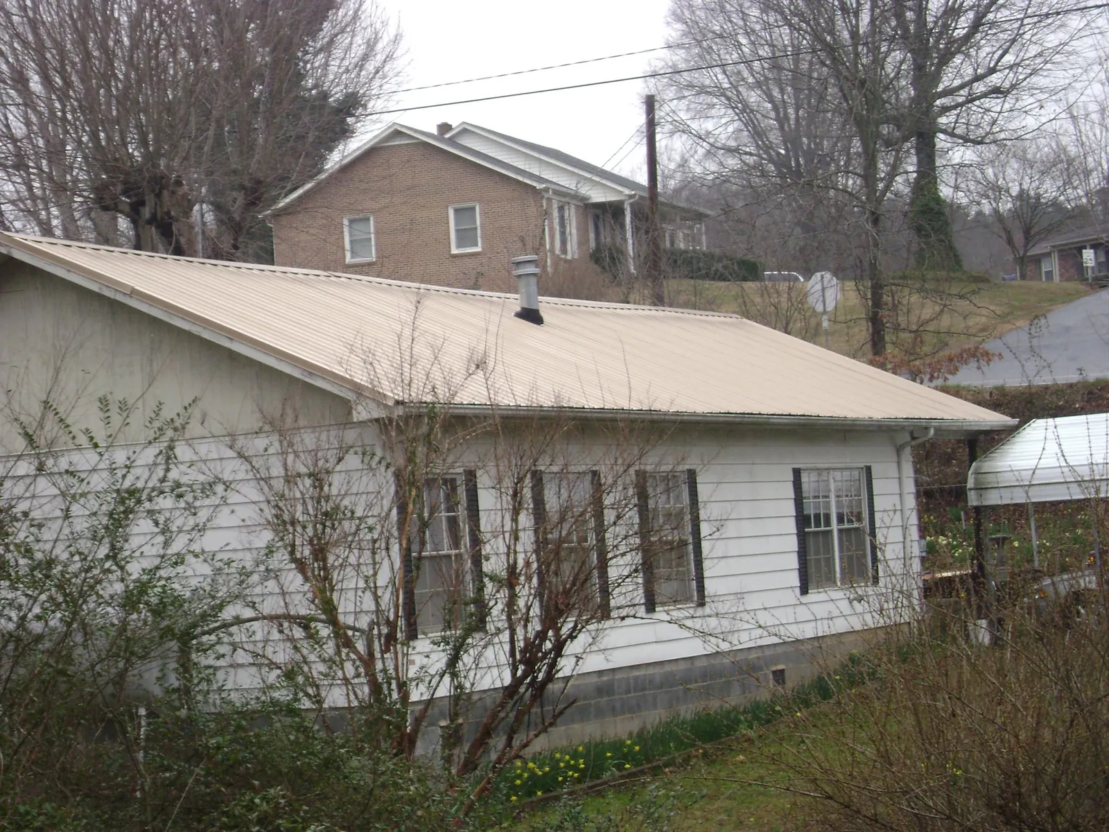 Tan metal roof on a white sided house set into a hillside — Commercial Roofing by Roofing Brothers in Haskell